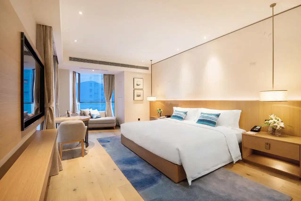 Modern hotel room with a large bed, seating area, and a large window.