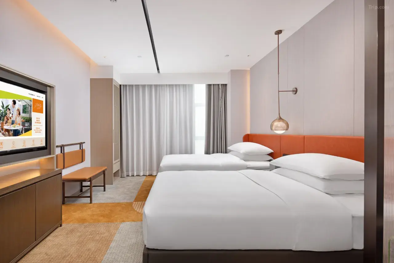 Modern hotel room with two twin beds, orange headboard, and wall-mounted TV.
