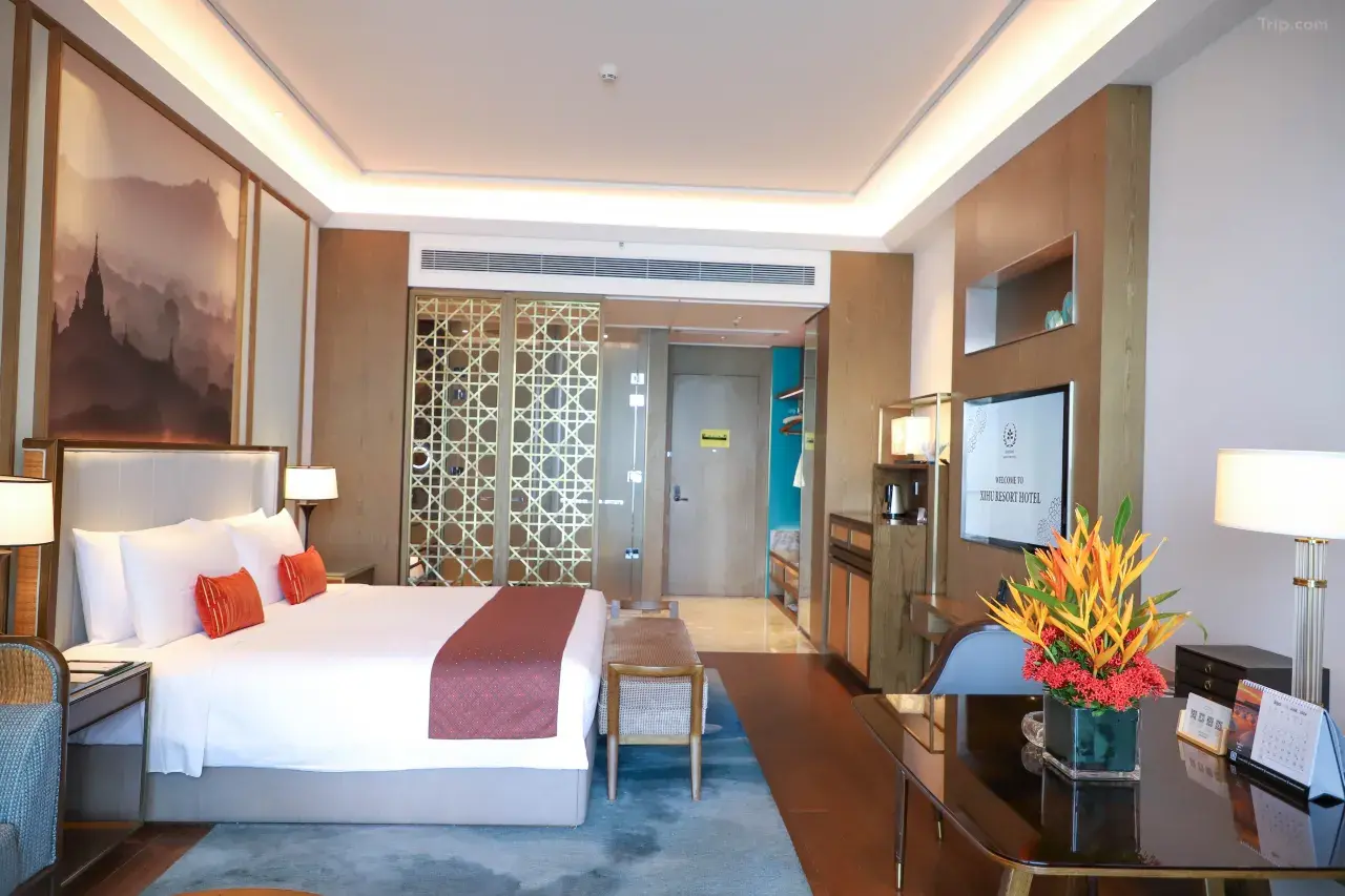 A luxurious hotel suite featuring a king-size bed, decorative gold lattice screen, and a modern desk with a colorful floral arrangement.