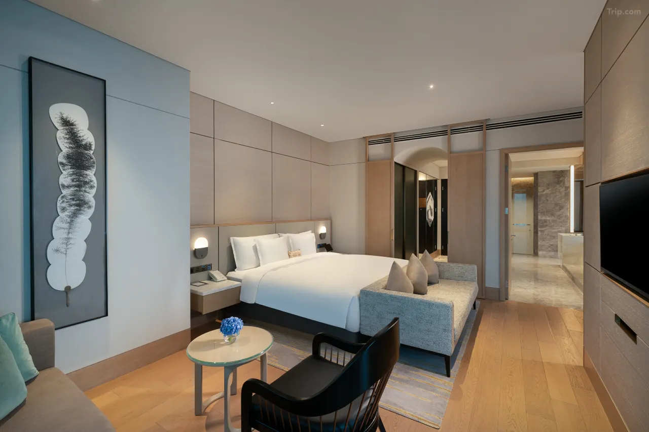 Modern hotel suite with a king bed, seating area, and minimalist decor.
