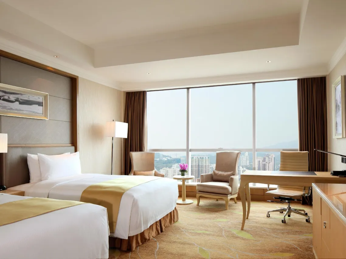 Twin beds hotel room with a city view, desk, and armchair.