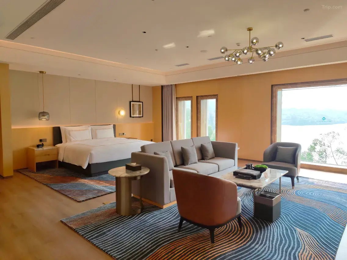 Luxurious hotel suite with a king-size bed, sofa, armchair, and a view of the lake.