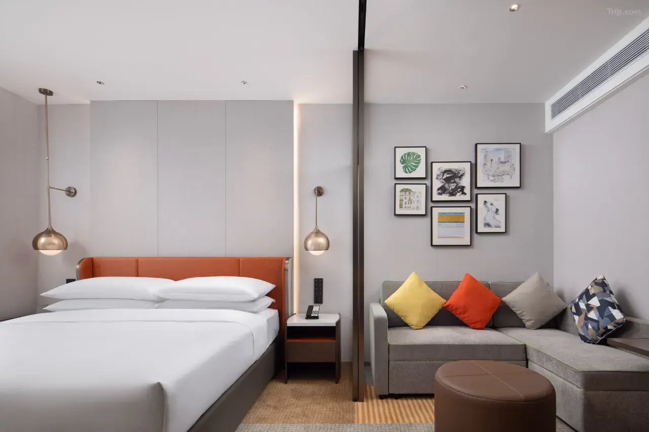 Modern hotel suite with a white bed and a grey sofa in a separate living area.