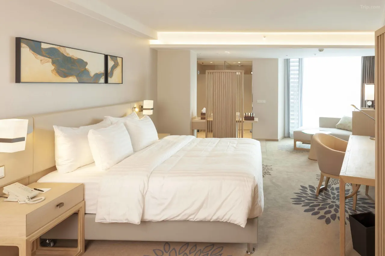 Modern hotel room with white bedding, wooden furniture, and a seating area.