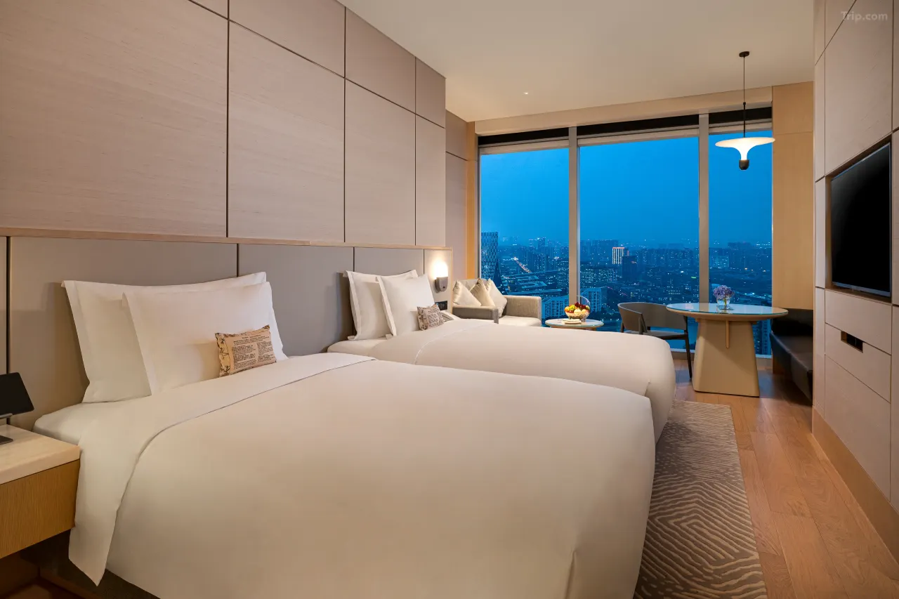 Modern hotel room with two twin beds and a city view at night.