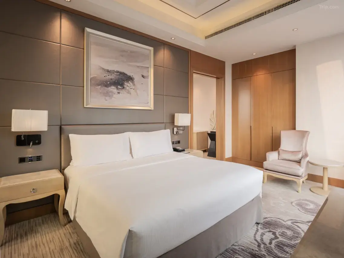 Luxury hotel room with king-size bed, abstract art, light wood furniture, and armchair.