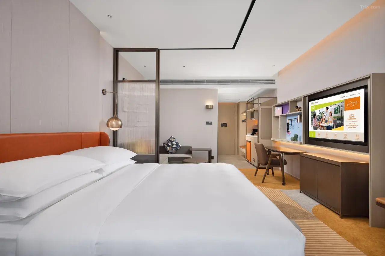 Modern hotel room with a king bed, desk, and large TV.