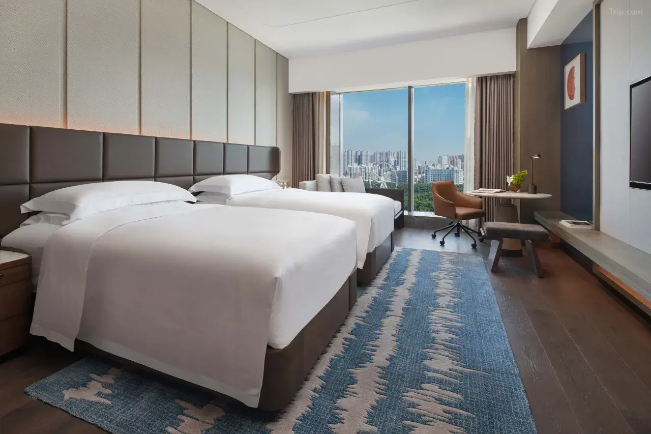 Modern hotel room with two twin beds, a desk, and a city view window.