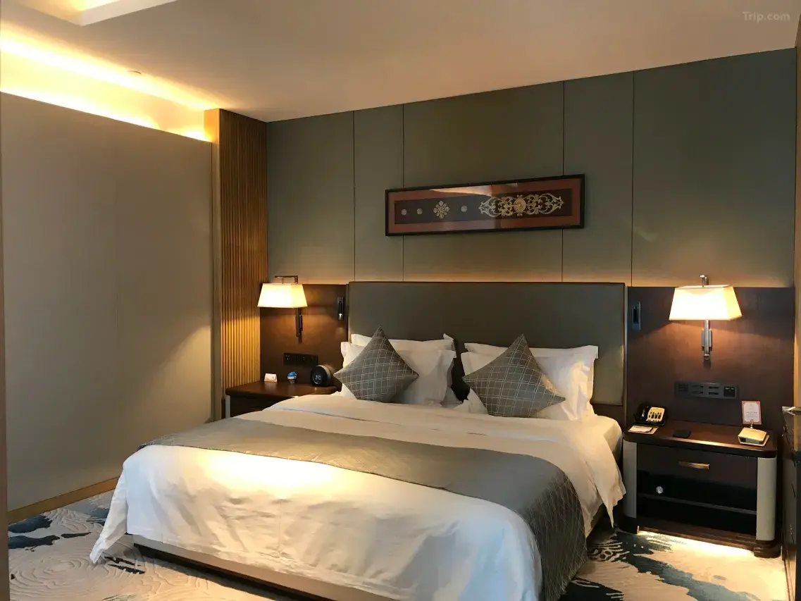 Modern hotel bedroom with warm lighting, a large bed, and elegant decor.