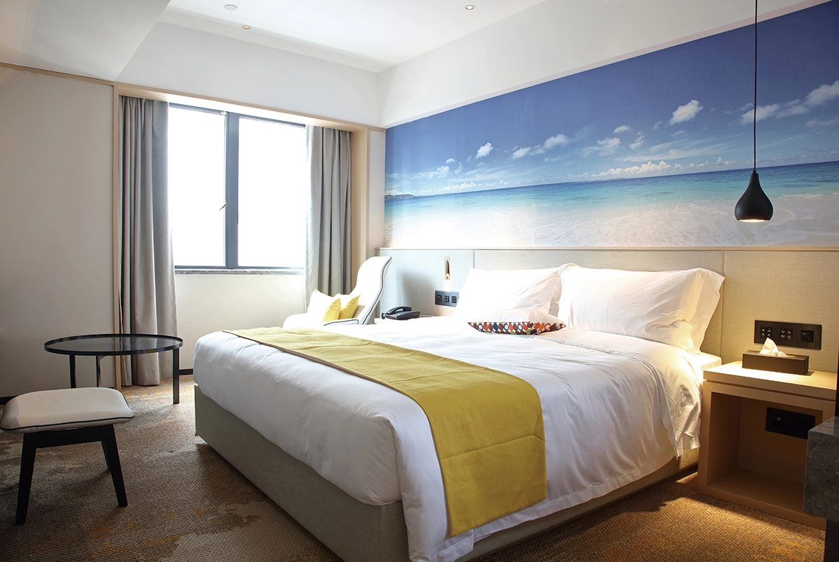 Modern hotel room with a large bed, beach mural, and window.