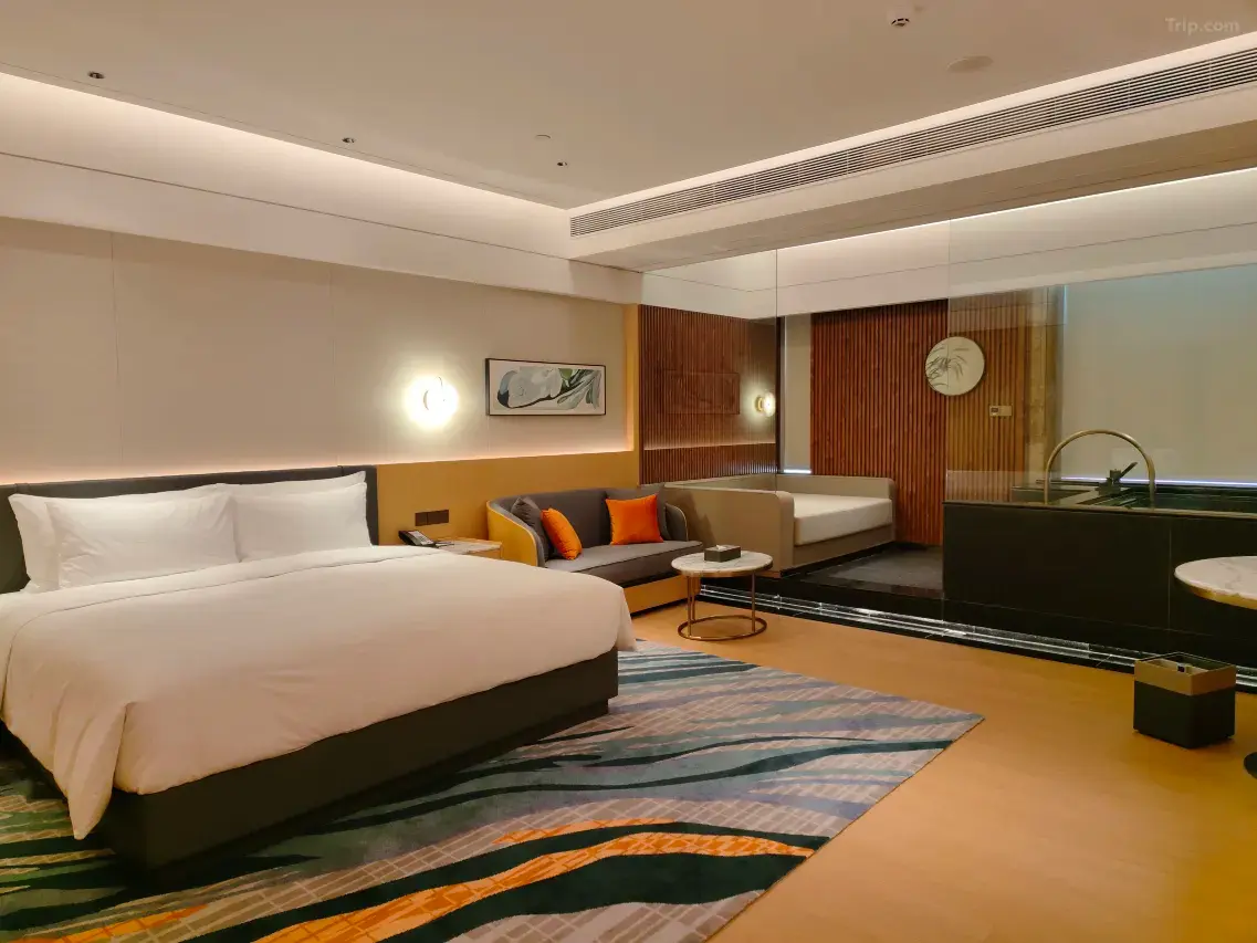 Modern hotel room with king bed, sofa, and glass-enclosed bathroom area.