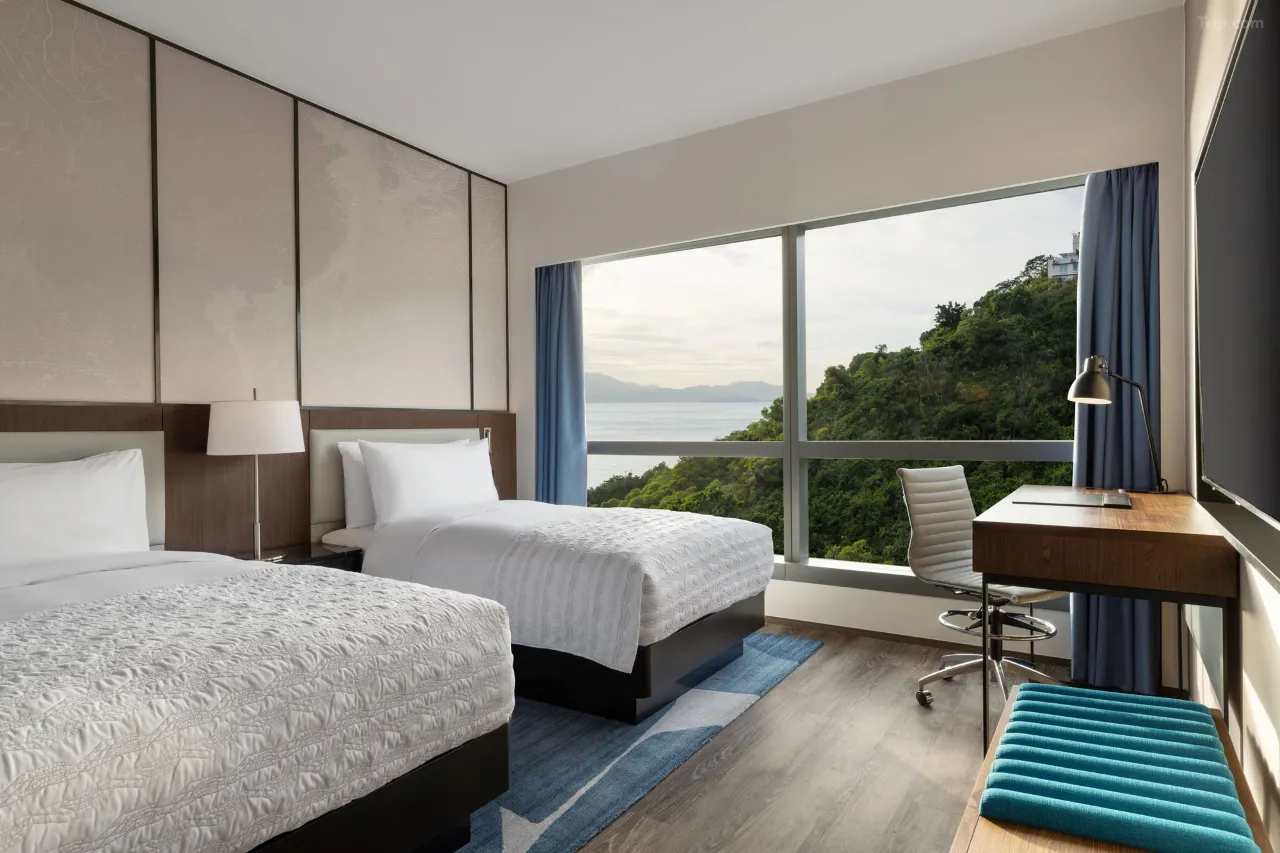 Modern hotel room with two twin beds and a scenic ocean and mountain view.