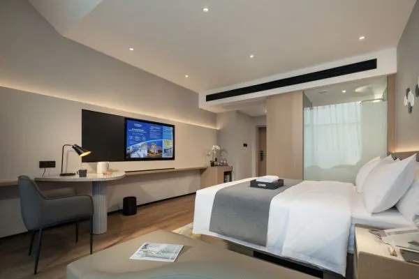 Modern hotel room with a king-size bed, large screen TV, and desk area.