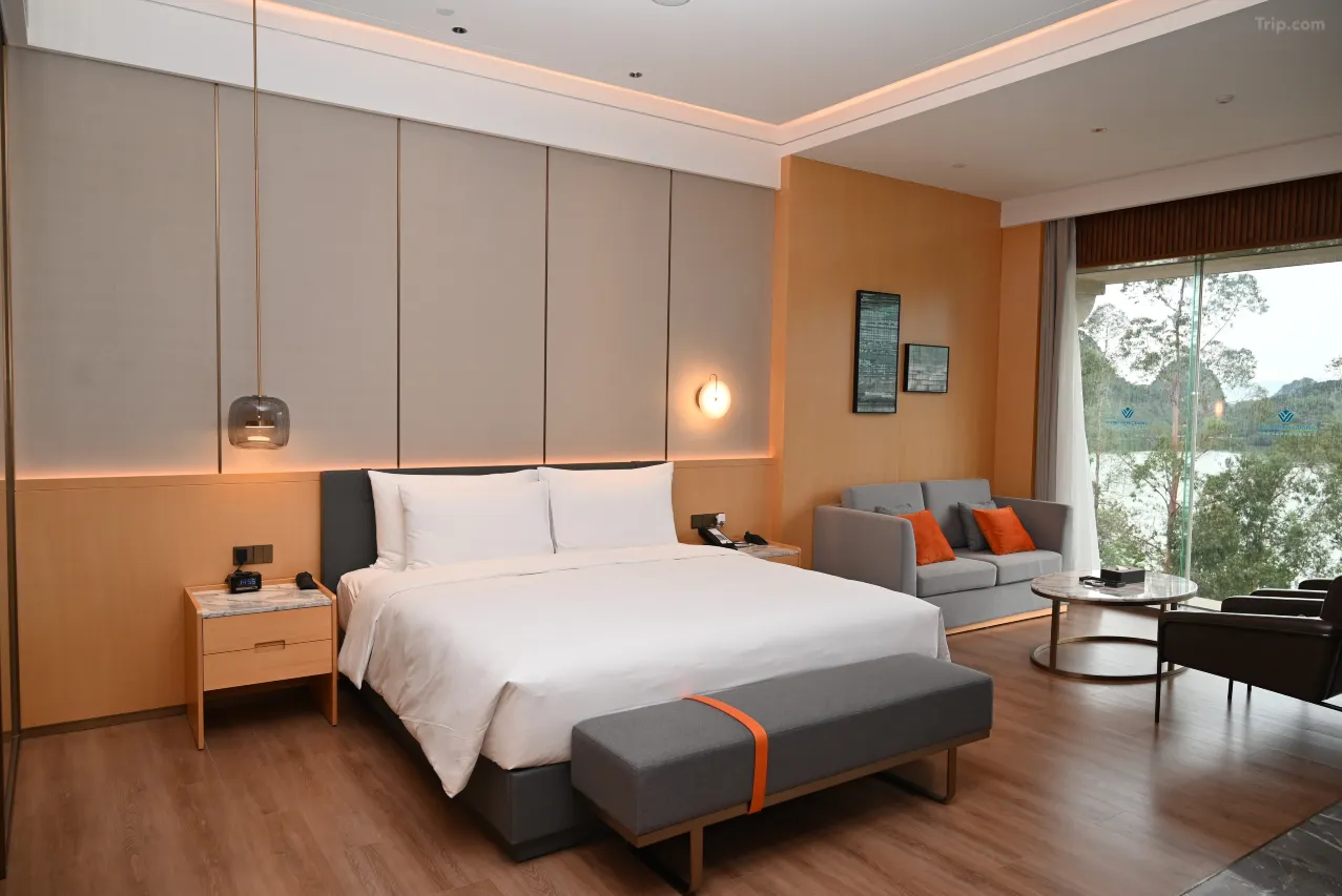 Modern hotel room with a large bed, seating area, and a window view of a lake and mountains.