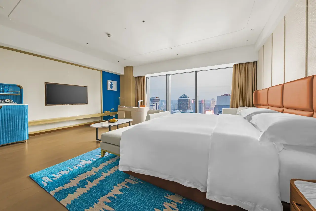 Modern hotel room with a city view, white bed, and blue accents.