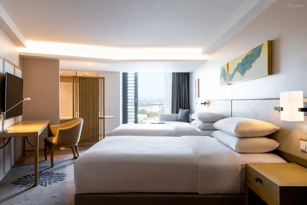 Modern hotel room with two twin beds, a desk, and large window with city view.