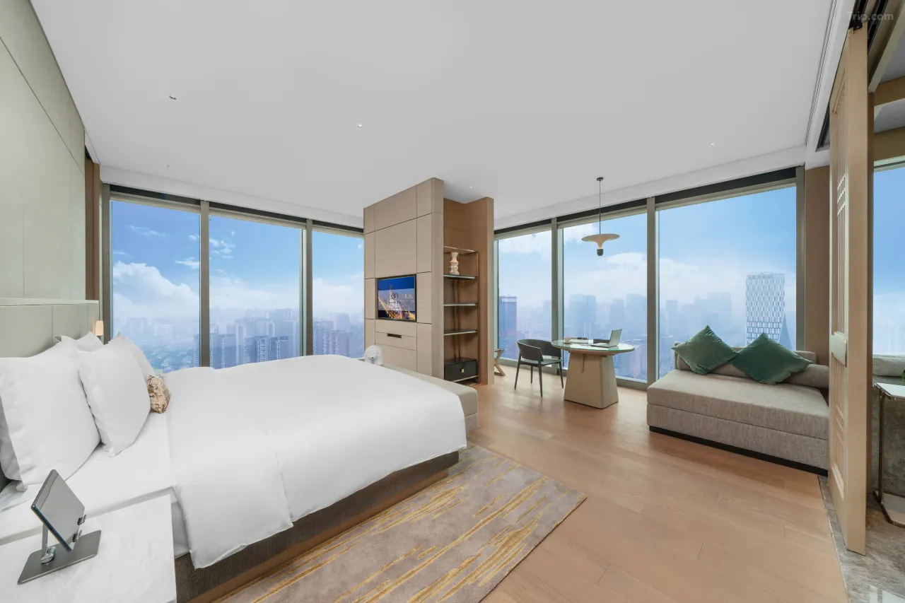 Modern hotel bedroom with floor-to-ceiling windows overlooking a city skyline.