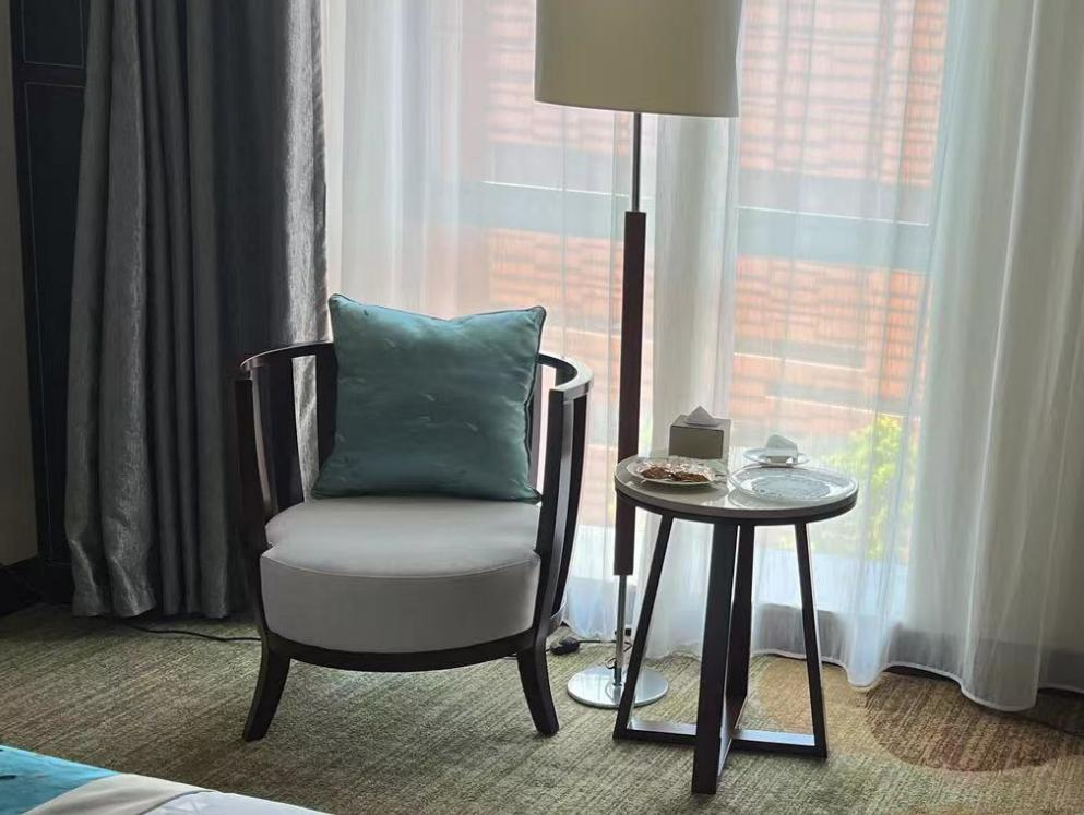 Armchair with blue cushion, floor lamp, and side table in a room with light-filtering curtains.