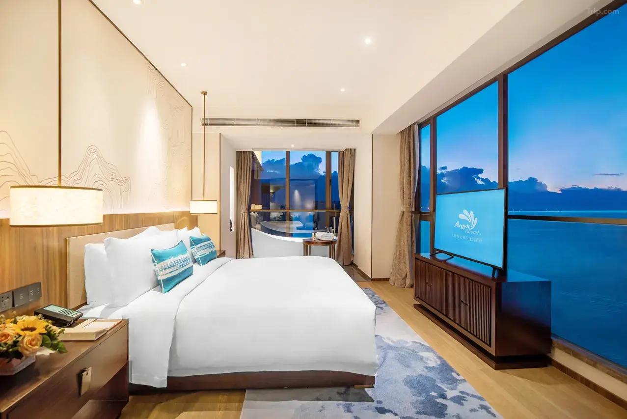 Luxurious hotel room with a large bed, ocean view, and a bathtub by the window.