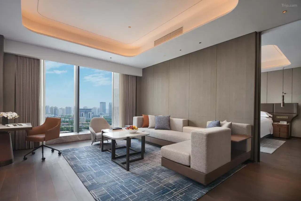 Modern hotel suite living room with city views and neutral decor.