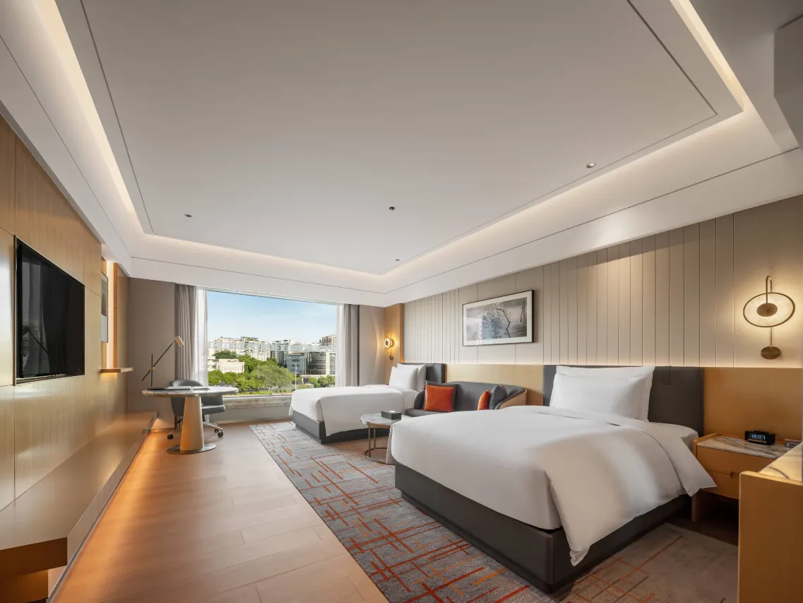 Spacious hotel room with two beds, a desk, and a city view from the large window.