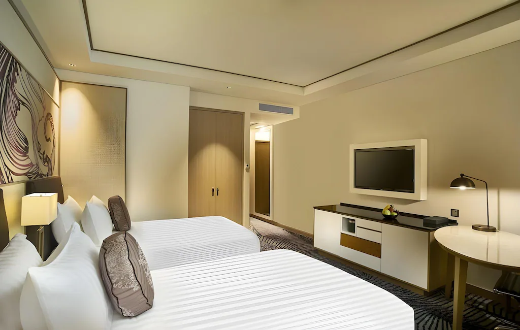 Hotel room with two beds, a TV, a desk, and neutral decor.