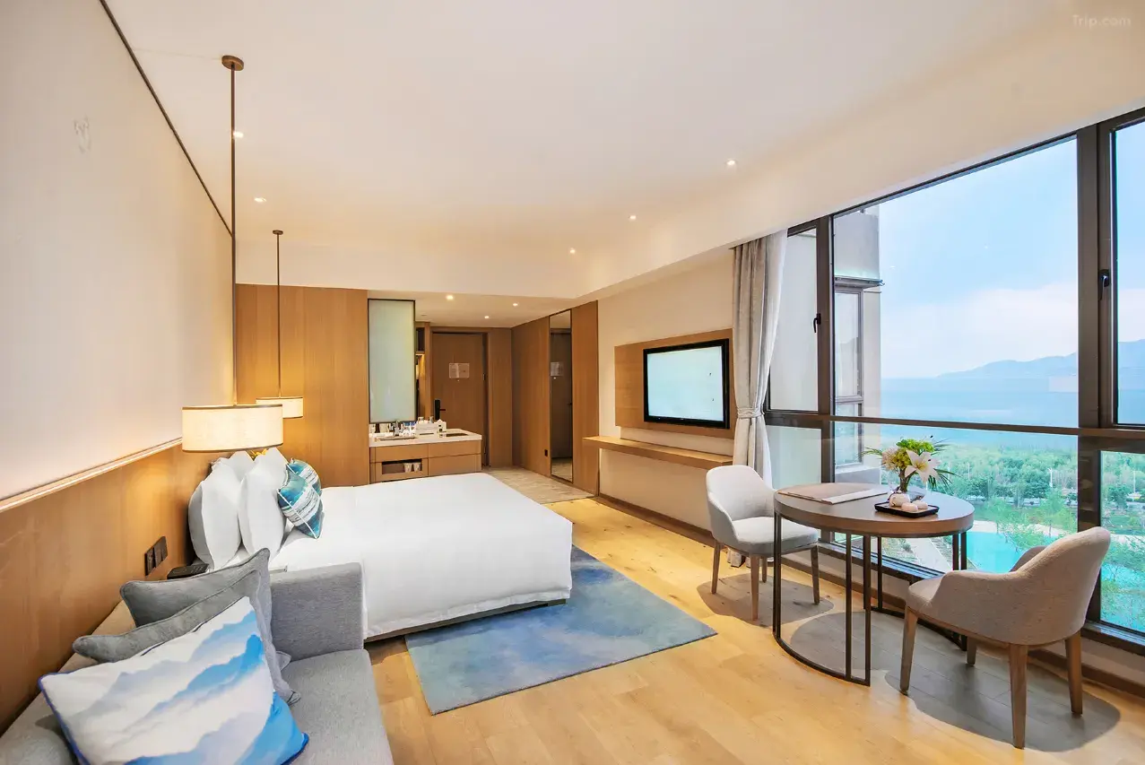 Spacious hotel room with a large bed, sofa, dining table, and a scenic view from the window.