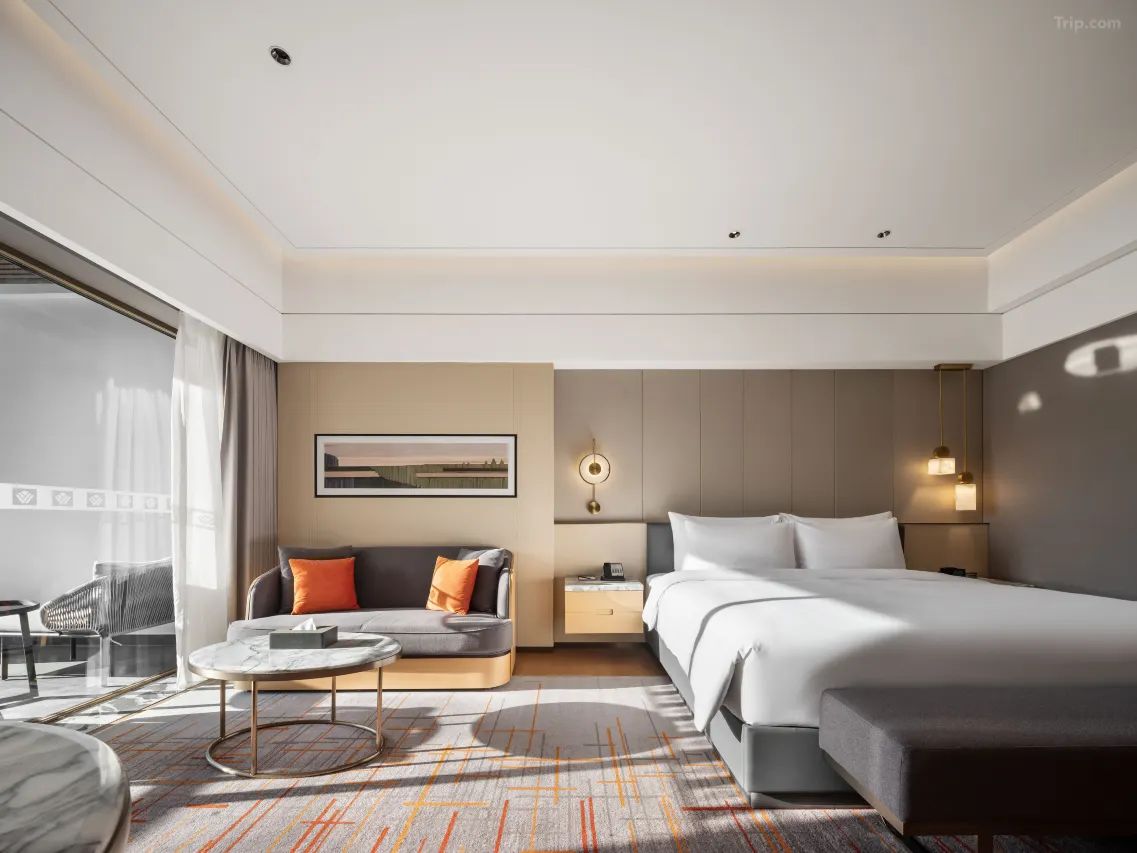 Modern hotel room with a large bed, sofa, coffee table, and balcony access.