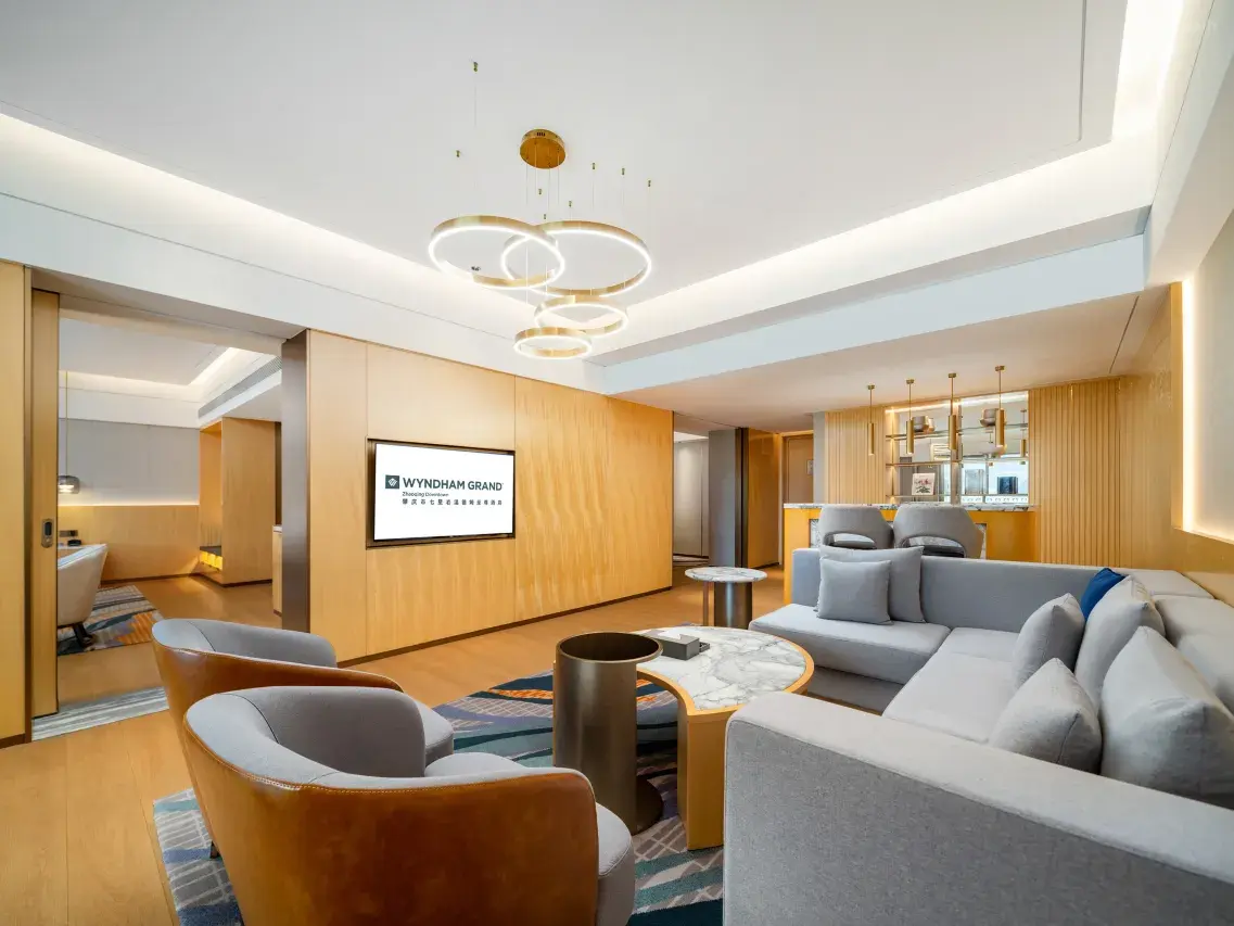 Spacious, modern hotel suite living room with light wood walls, gray sofas, and round chandelier.