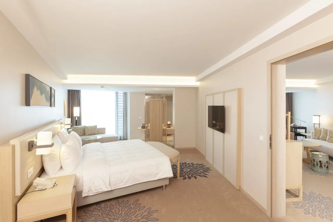 Modern hotel suite with a king bed, seating area, and neutral decor.
