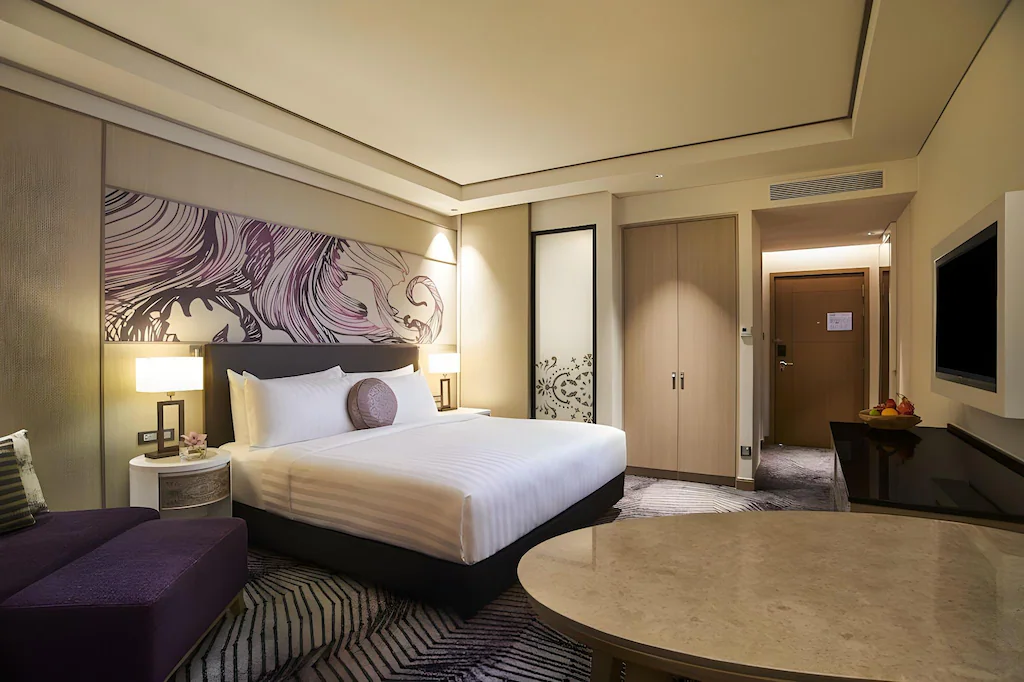 Hotel room with king bed, decorative headboard, and purple chaise lounge.