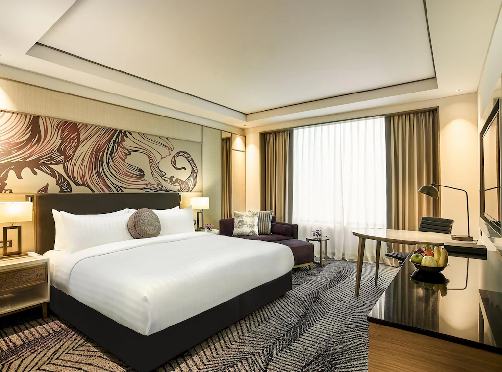 Hotel room with king-size bed, chaise lounge, desk, and patterned carpet.