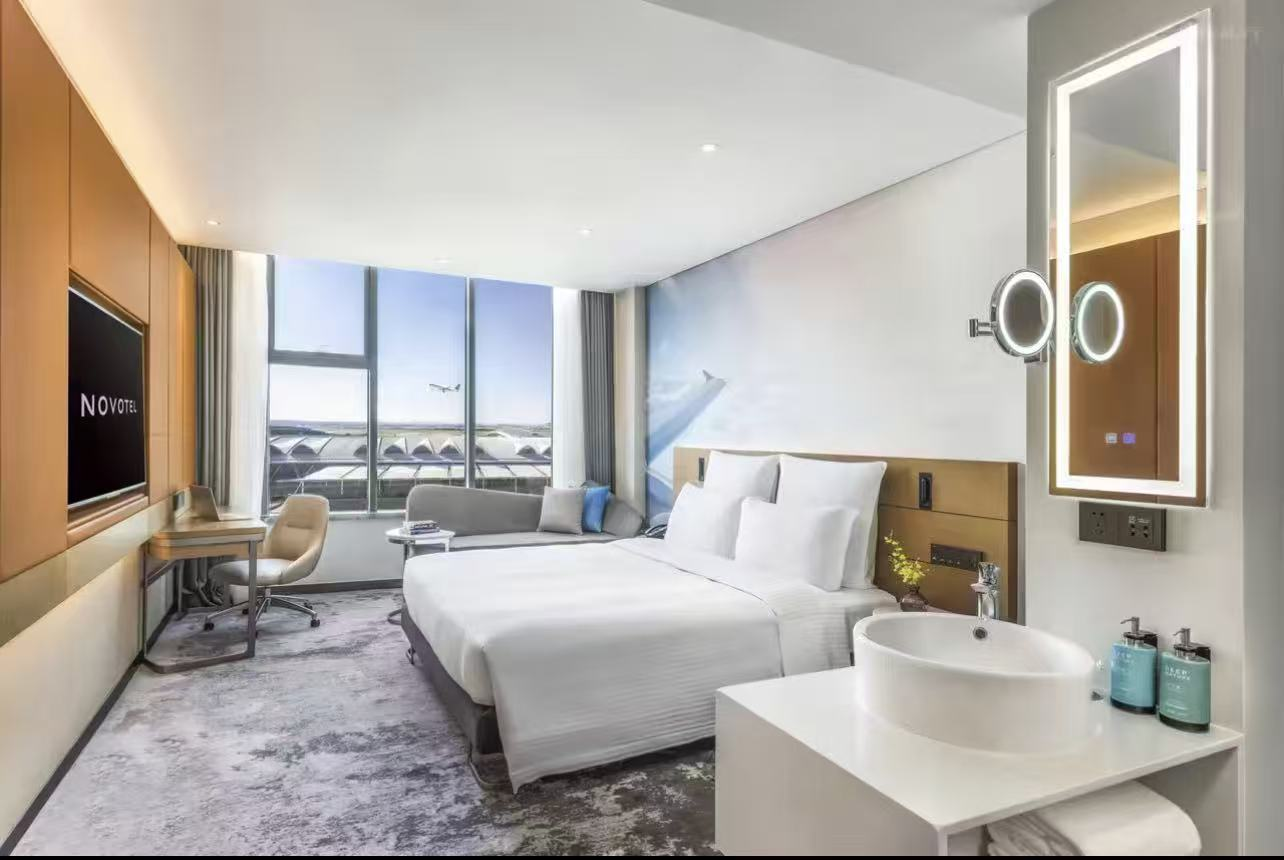 Novotel hotel room with runway view, bed, desk, and modern bathroom.