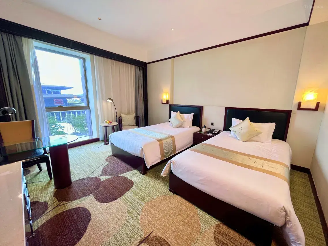 Hotel room with two single beds, a desk by the window, and floral carpet.