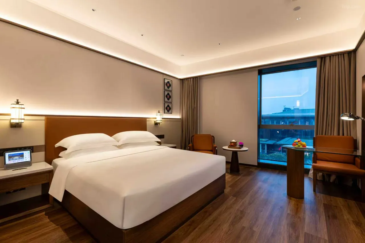 Hotel room interior with king-size bed, desk, and city view.