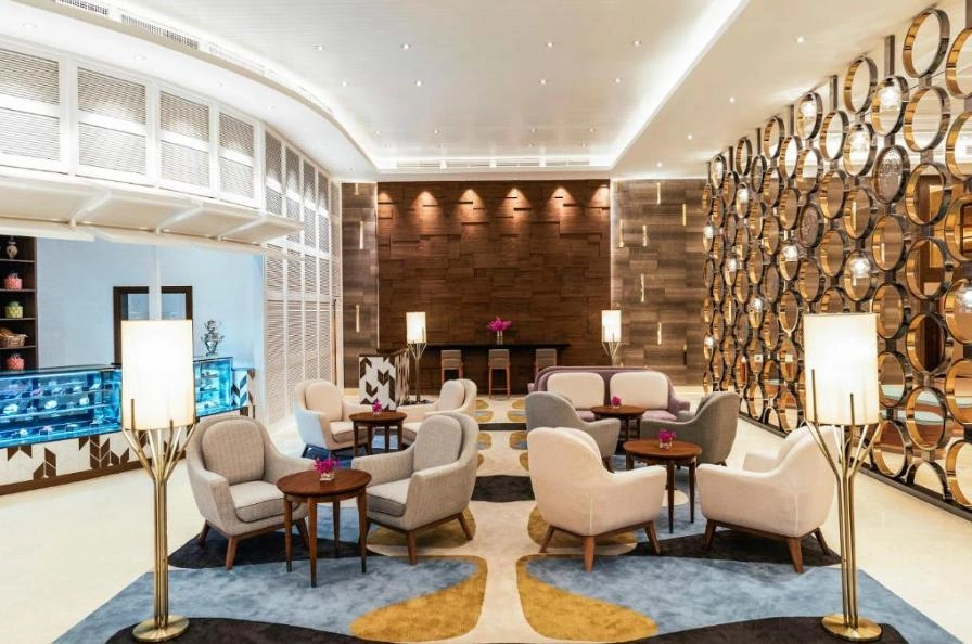 Elegant hotel lobby with seating areas, decorative walls, and a pastry display.
