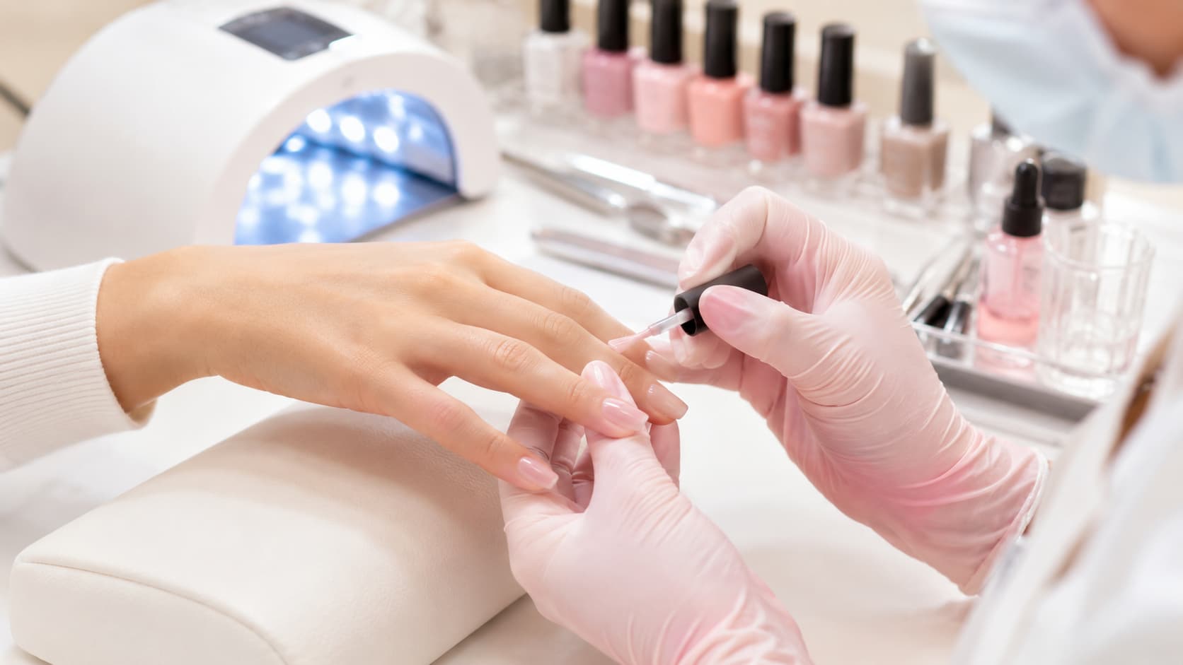 Professional nail technician applying sheer jelly gel polish safely under salon conditions with LED UV lamp