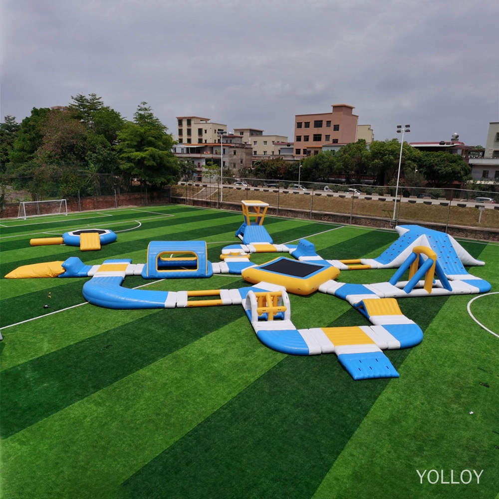 Ein Bild eines aufblasbaren Wasserparks mit verschiedenen Funktionen wie Rutschen, Trampolinen und Hindernisparcours. Er steht auf einer grünen Wiese mit Bäumen und Gebäuden im Hintergrund.