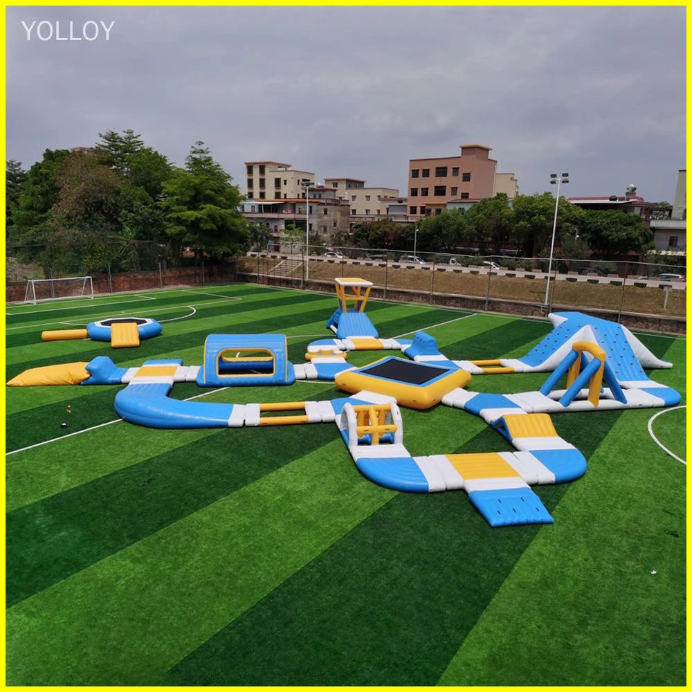 Image d&#39;un parc aquatique gonflable avec diverses fonctionnalités telles que des toboggans, des trampolines et des parcours d&#39;obstacles. Il est installé sur un terrain vert avec des arbres et des bâtiments en arrière-plan.