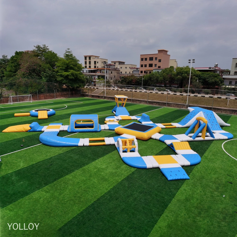 Uma imagem de um parque aquático inflável com vários recursos, como escorregadores, trampolins e pistas de obstáculos. Ele é montado em um campo verde com árvores e prédios ao fundo.