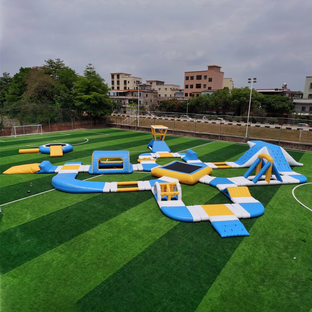 Ein Bild eines aufblasbaren Wasserparks mit verschiedenen Funktionen wie Rutschen, Trampolinen und Hindernisparcours. Er steht auf einer grünen Wiese mit Bäumen und Gebäuden im Hintergrund.