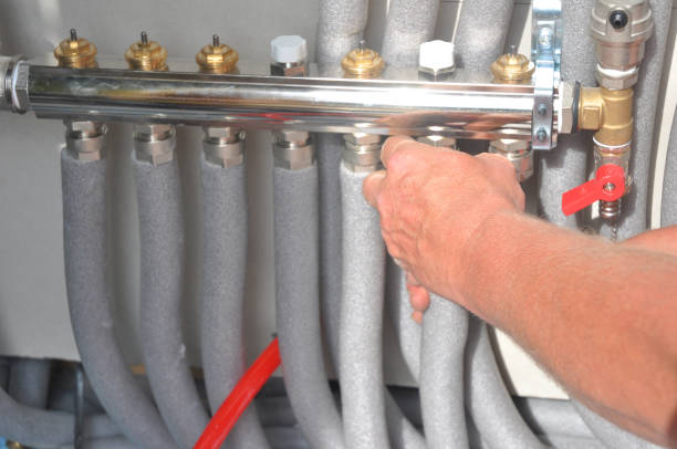 Close-up of a plumber's hand adjusting valves on a manifold system with insulated pipes.