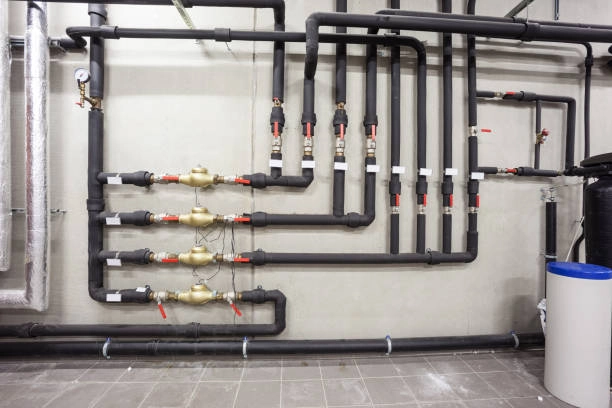 Complex network of insulated pipes and valves on a concrete wall, possibly part of a building's plumbing or heating system. - FUNAS