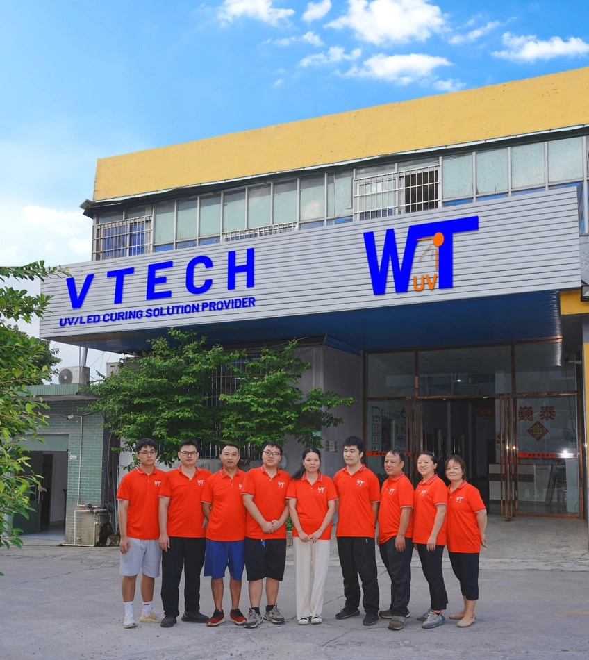 The image shows a group of people in red shirts standing in front of a building. The building has a sign that says "VTECH UV/LED CURING SOLUTION PROVIDER".