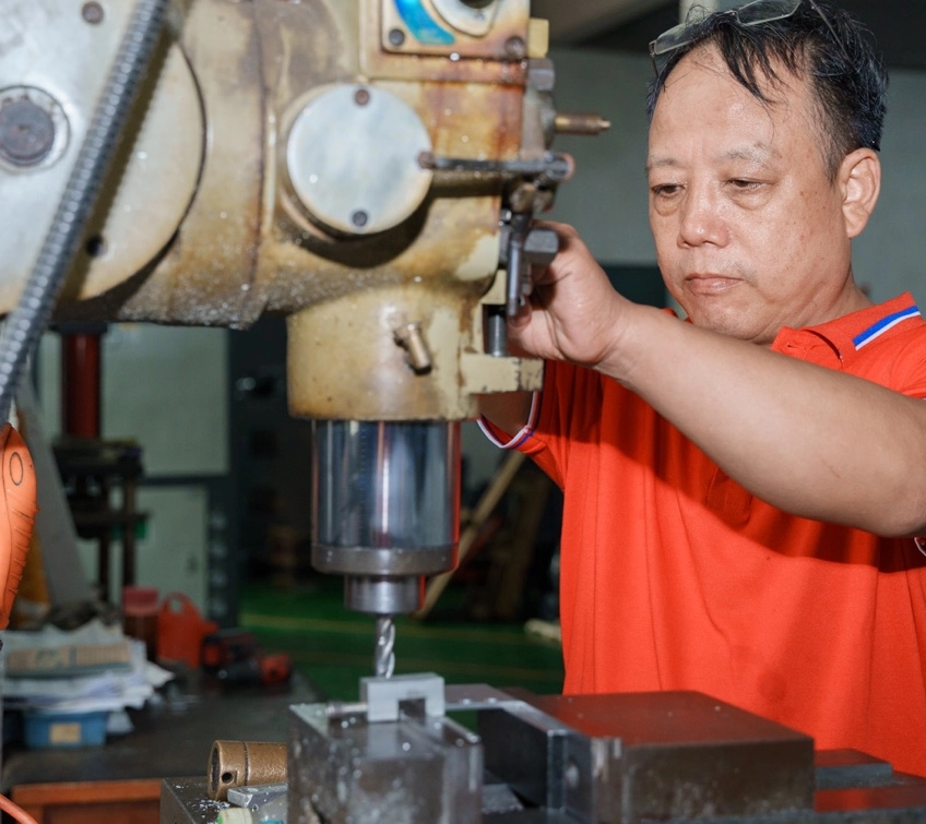 Wtjd-A-man-in-a-red-shirt-is-operating-a-drill-press-in-a-machine-shop. Wtjd A man in a red shirt is operating a drill press in a machine shop.