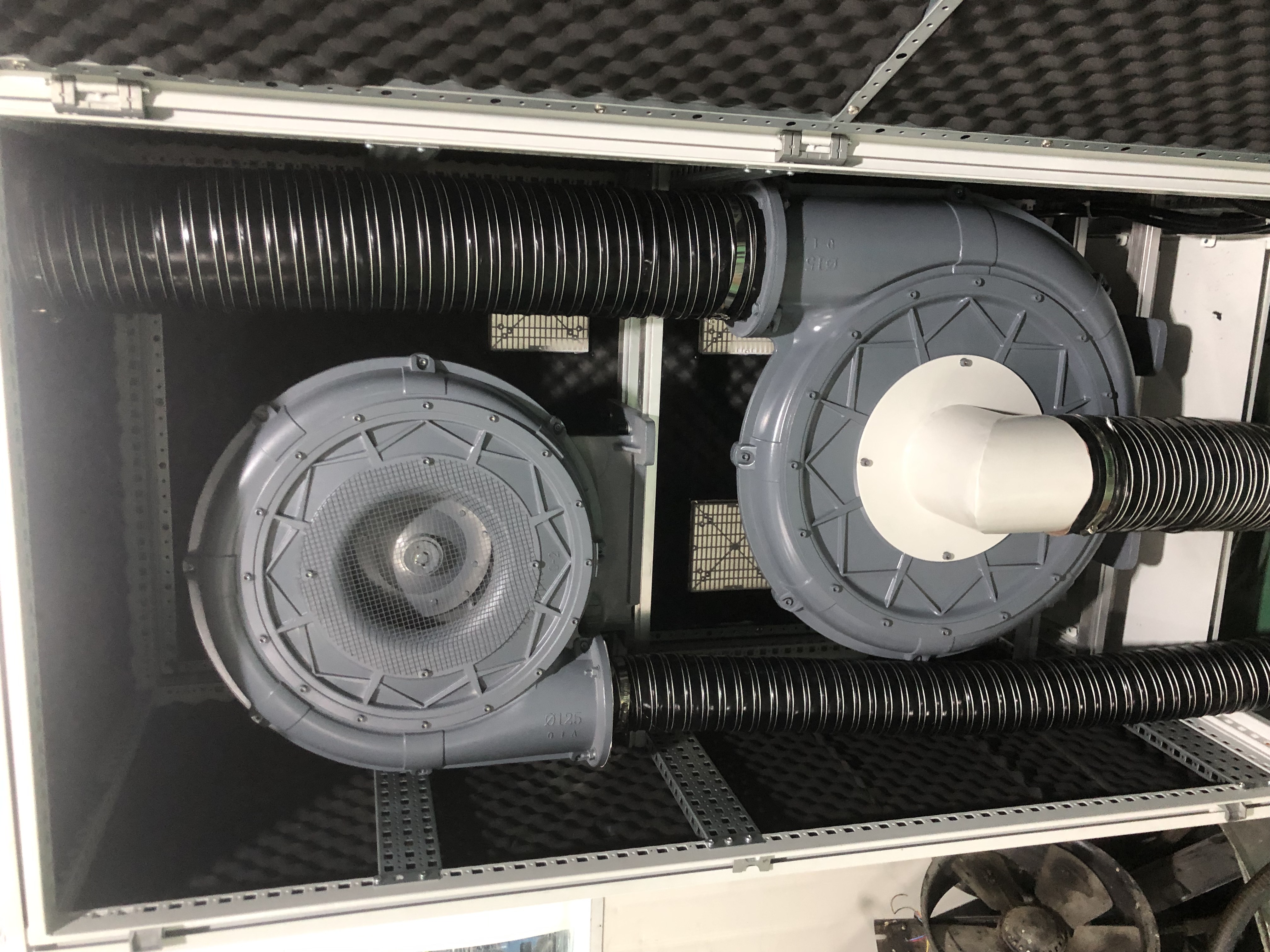 Here's a descriptive alt text for the image:

"Interior view of a soundproofed enclosure containing two industrial blowers with flexible ducting, mounted on a rack system with sound dampening material."