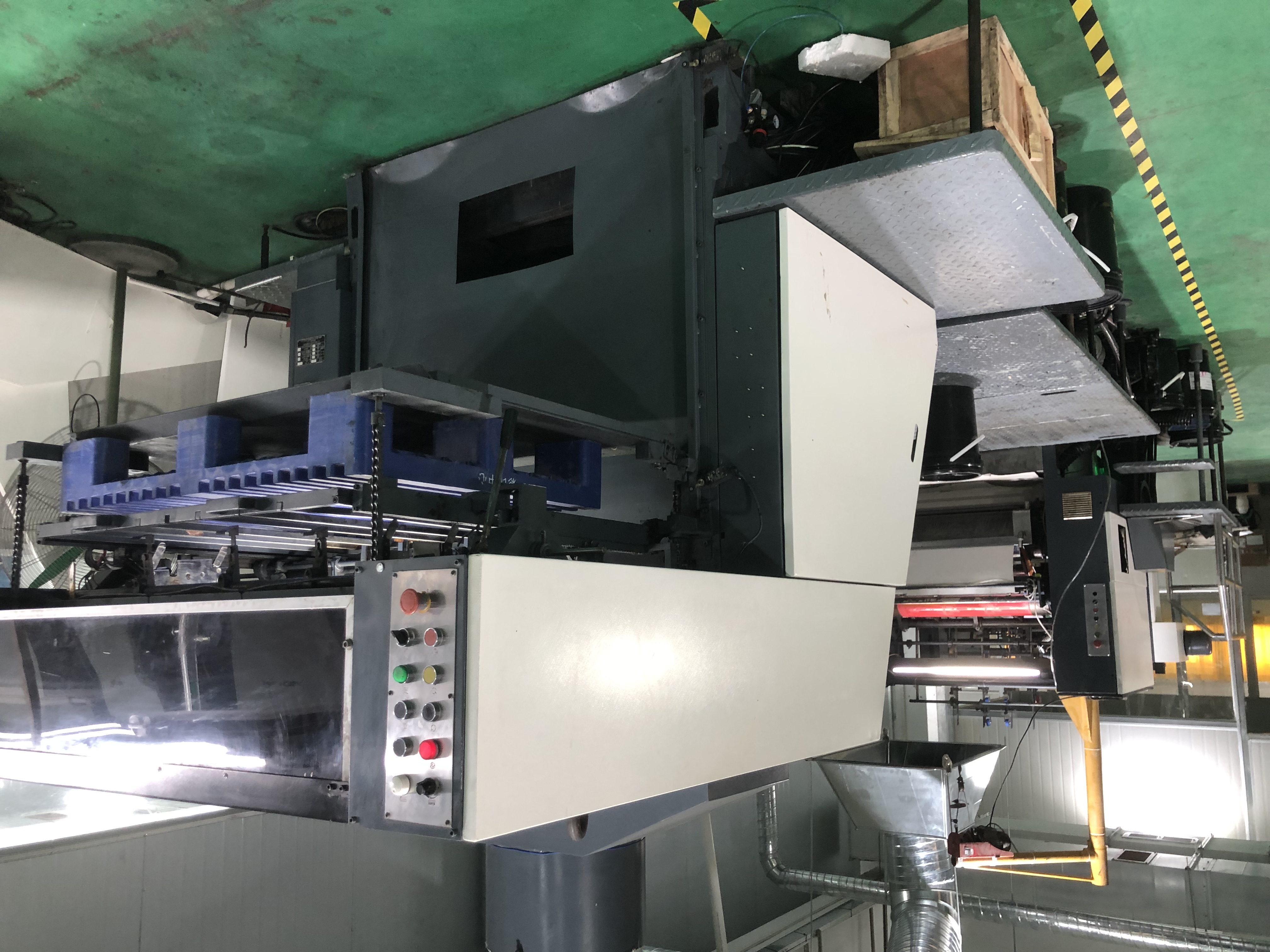 High-angle view of a large industrial printing press with a control panel and a pallet of materials.