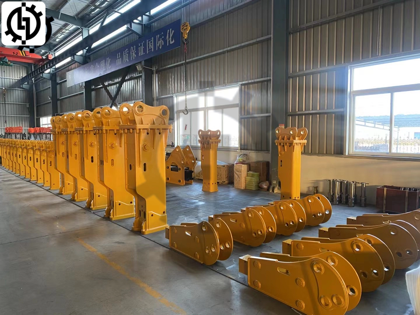 Huilian-rock-breaker-factory Rows of newly manufactured yellow hydraulic rock breakers stand in the Huilian rock breaker factory. Various components are also visible, showcasing the factory's production process.