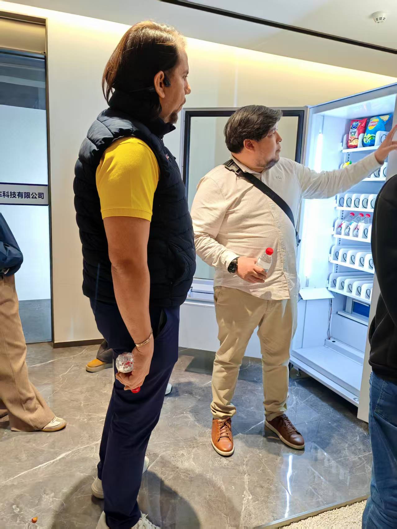 Two men inspecting snacks and drinks inside a MAKMIK Refrigerated Vending Machine.