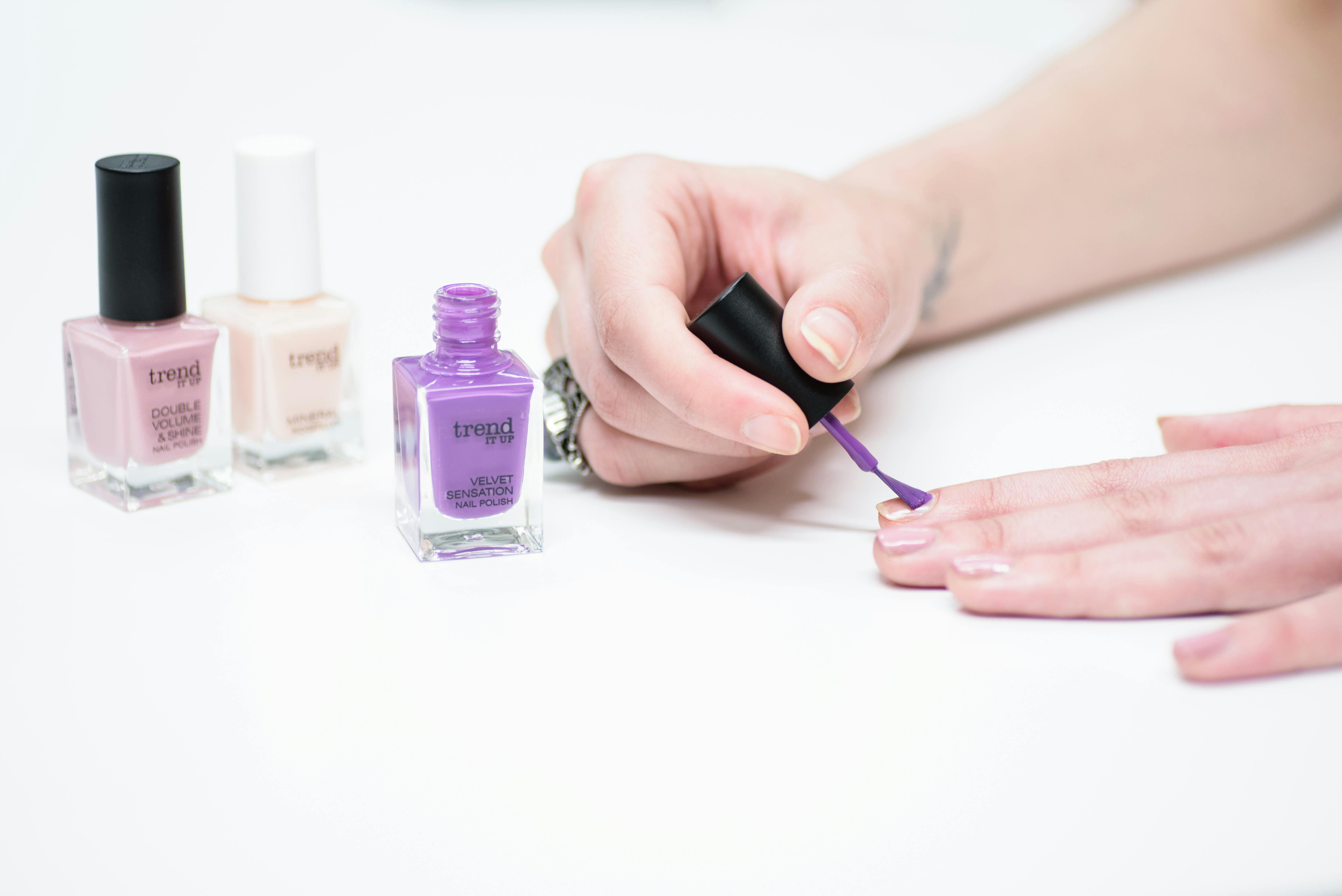 A woman applying purple nail polish with bottles of various colors in the background. A woman applying purple nail polish with bottles of various colors in the background.